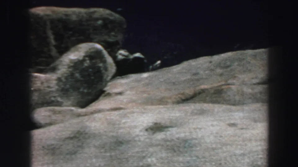 1969 Lake Tahoe 8mm frame showing rounded granite boulders, shaded trees, and a sloping rocky surface.