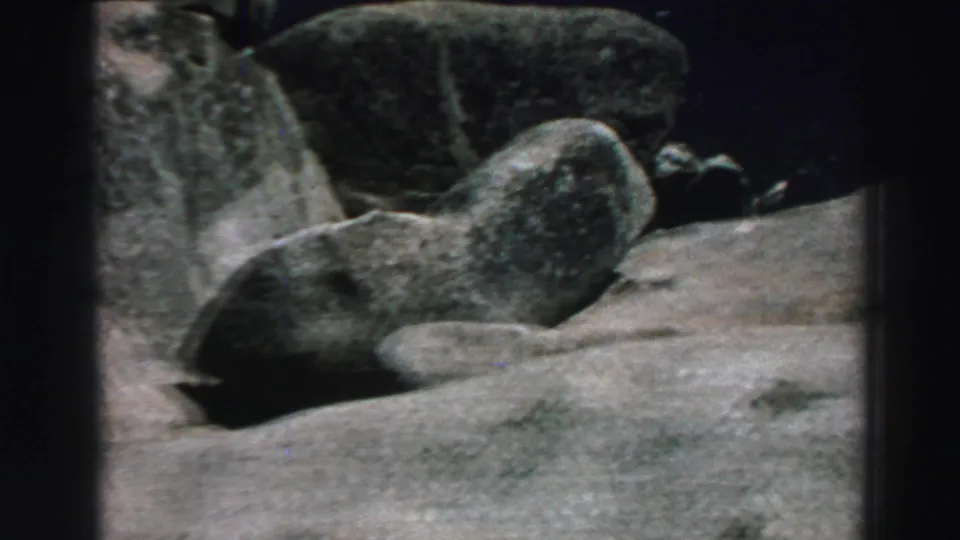 1969 Lake Tahoe home-movie frame showing close gray boulders and pale granite-like rock surfaces in natural light.