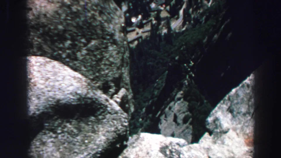 1969 Lake Tahoe home-movie view looking down over rocks, trees, and a distant blue-shirted hiker in the mountain terrain.
