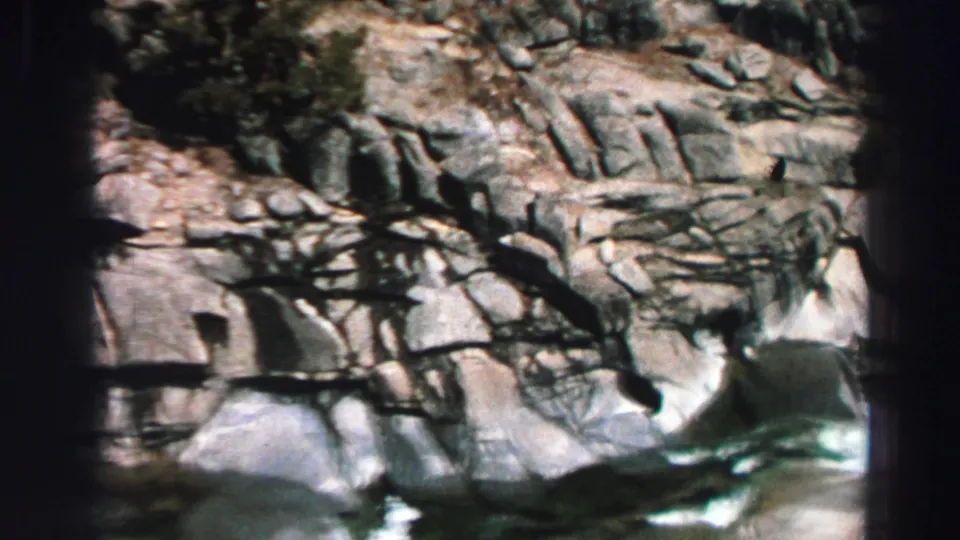 1969 Lake Tahoe frame showing pale rock formations, bare branches, and a small rushing water feature below.