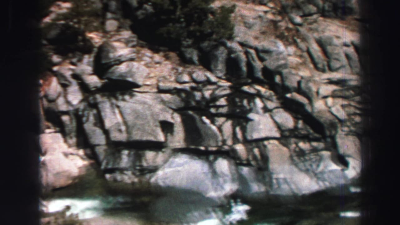 Rocky stream channel with granite walls, evergreen shadows, and whitewater at the bottom of the frame.