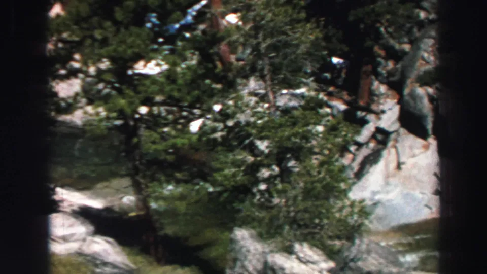 1969 Tahoe scenic frame where trees partly cover pale granite and a small stream running through the rocks.