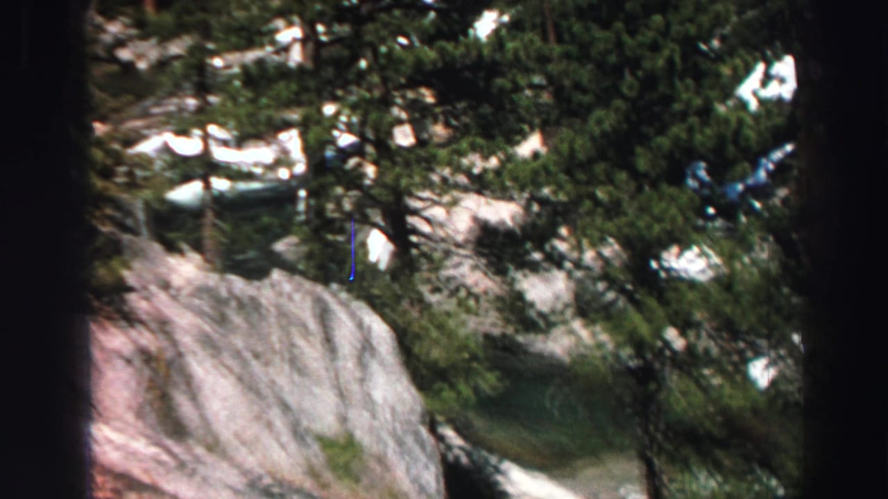 Evergreen trees and pale rocky slope with patches of snow.
