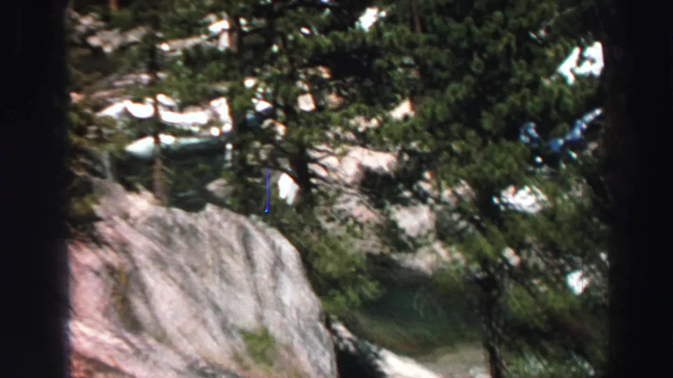 1969 Lake Tahoe home-movie frame showing evergreen branches over a steep granite slope with scattered snow patches.