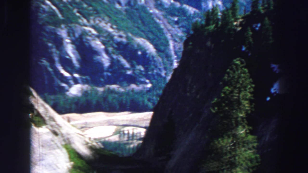 Forest foreground opening onto pale rock slopes and a mountain valley beyond.