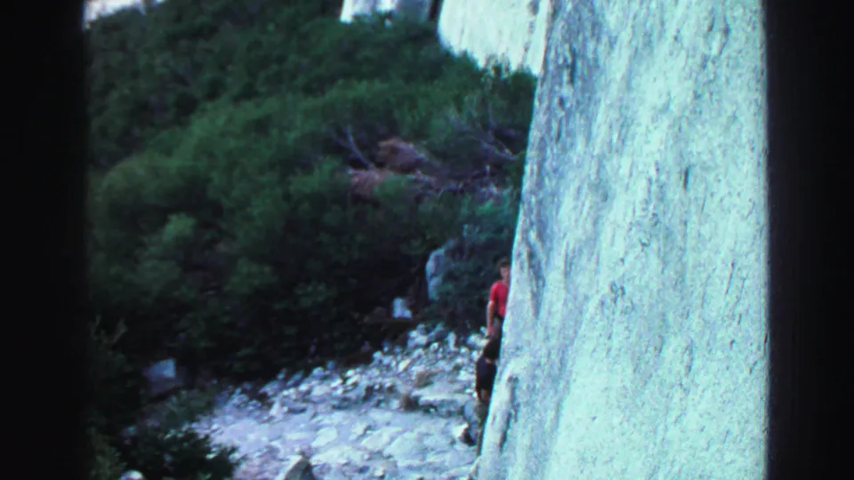 1969 Lake Tahoe trail view with a partly visible hiker in red beside a pale rock wall and brush.