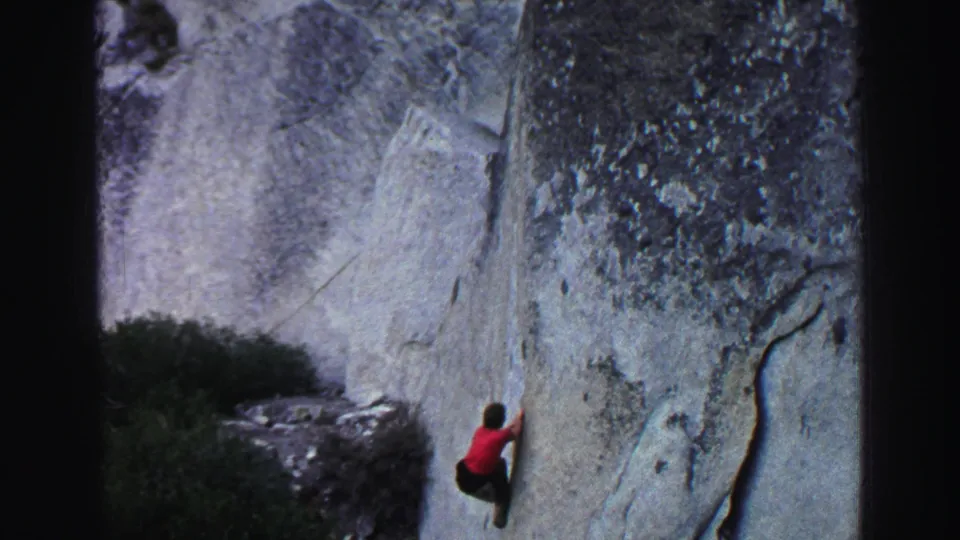 1969 Lake Tahoe 8mm frame showing the climber low on the granite wall, with surrounding brush and textured rock visible.