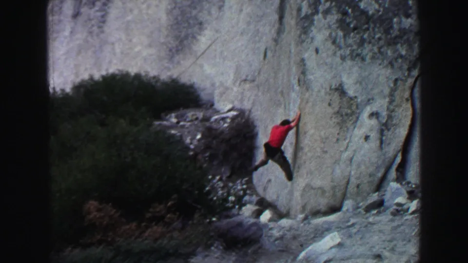 1969 Lake Tahoe 8mm frame of the red-shirted climber extending one leg while moving across a steep granite face.