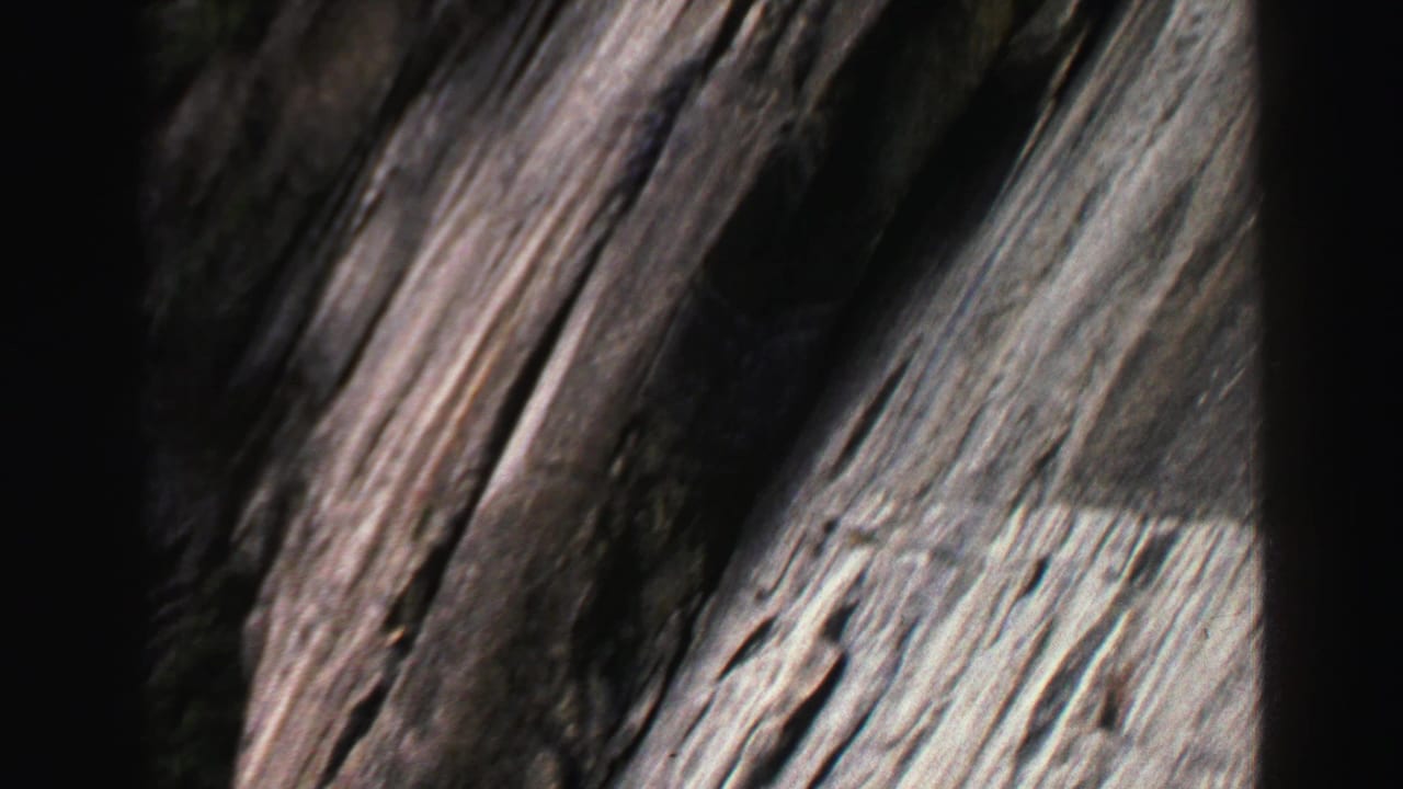 Close view of dark gray layered cliff rock with deep vertical cracks.