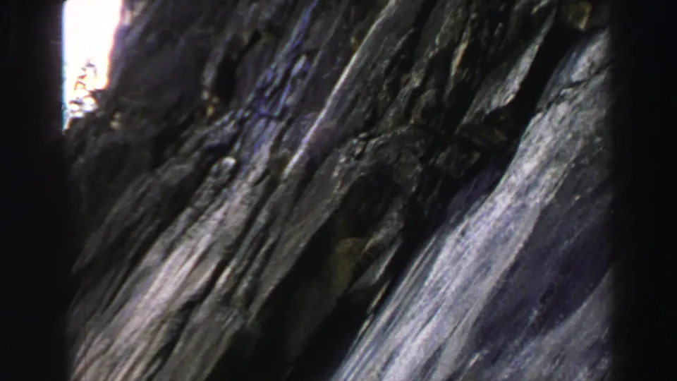 A Lake Tahoe cliff face appears in a 1969 8mm frame, with dark stone, a narrow vertical gap, and bright sky at the top.