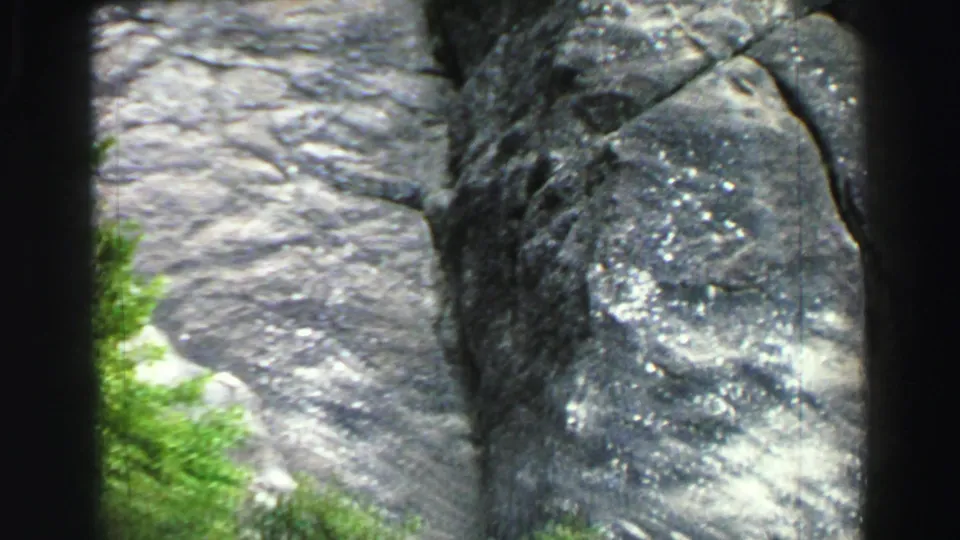 A 1969 Lake Tahoe 8mm frame shows gray rock slabs, a darker weathered face, and small green foliage at the base.