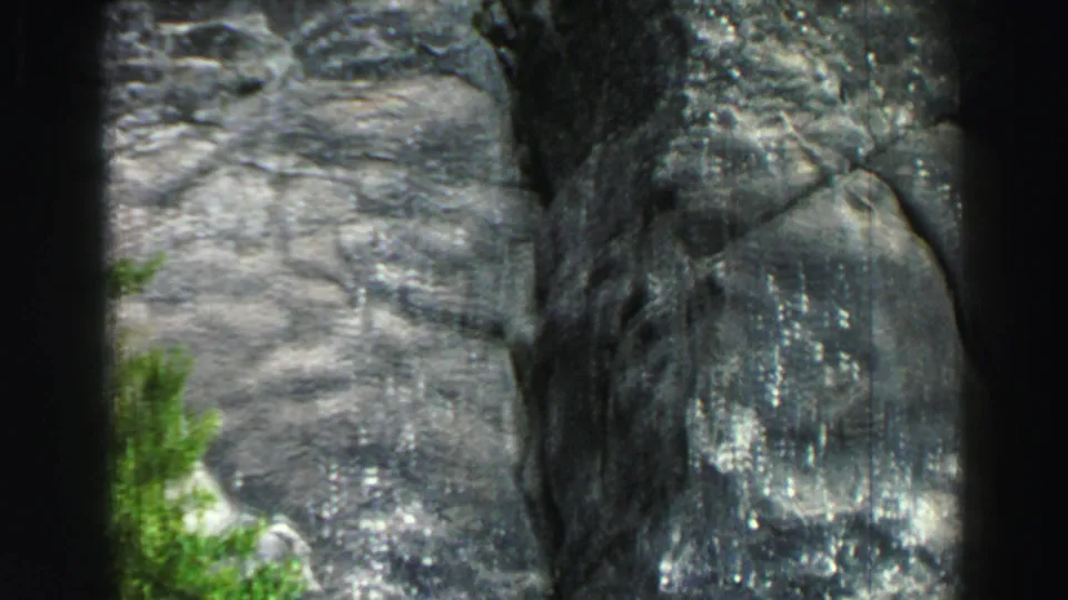 1969 Lake Tahoe home-movie frame showing a close view of gray granite canyon walls, small green plants, and dark 8mm frame edges.