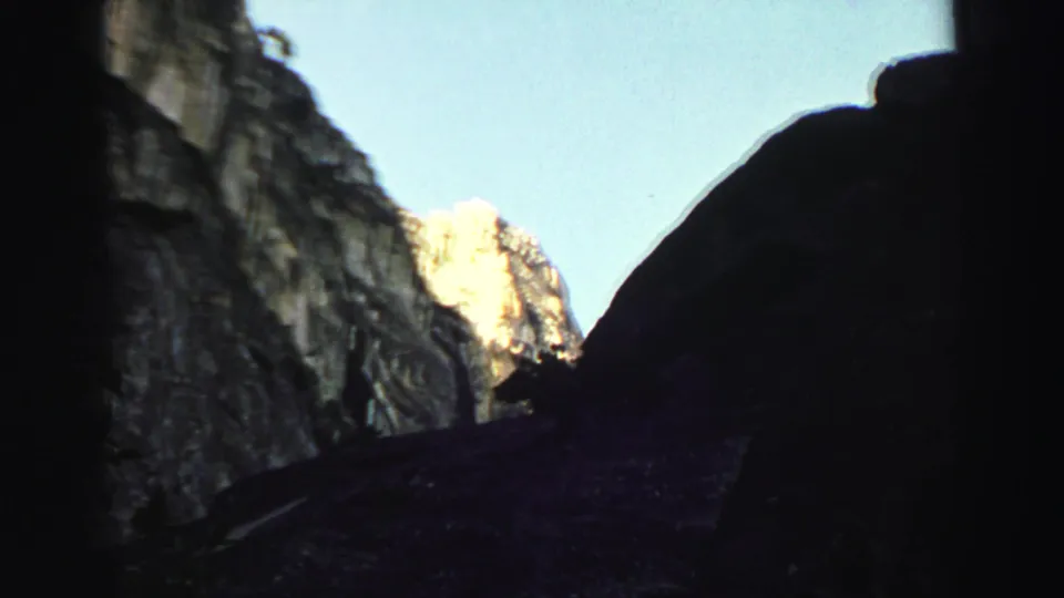 Lake Tahoe mountain canyon frame with dark foreground cliffs, pale blue sky, and a distant sunlit peak revealed by the upward camera pan.