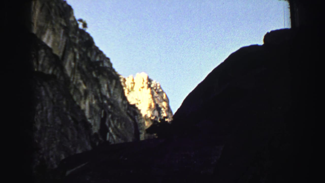 Dark canyon opening with sunlit mountain rock visible beyond shadowed cliffs.