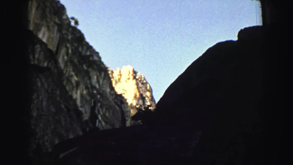 1969 Lake Tahoe area home-movie frame looking from a dark rocky passage toward a bright mountain face and blue sky.