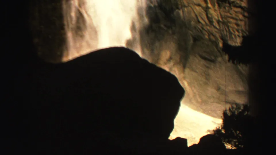 Late-1960s Lake Tahoe area frame showing a bright waterfall falling past a large dark rock silhouette and steep stone wall.