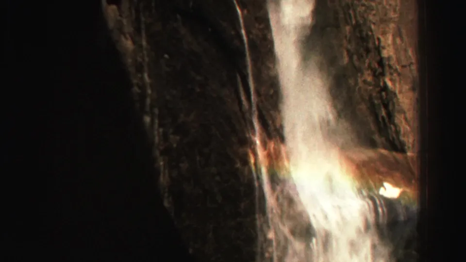Lake Tahoe area 1969 home-movie frame showing a vertical waterfall, bright mist, and deep shadows along the surrounding rock walls.