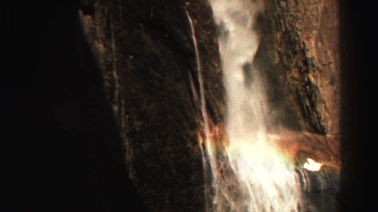 Waterfall drops down a dark rocky cliff with a faint rainbow in the mist.