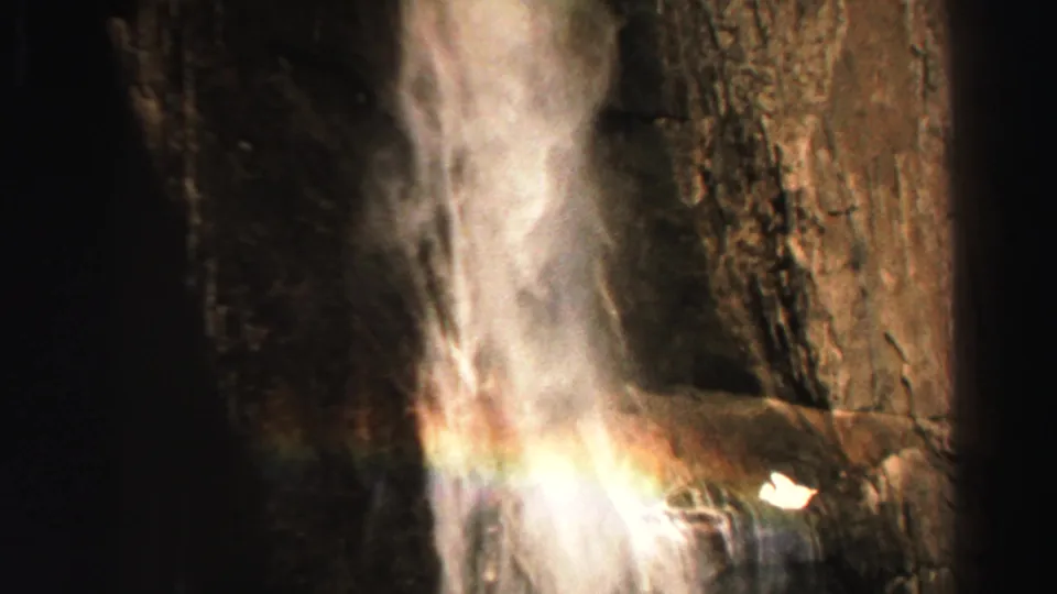 Lake Tahoe waterfall frame from 1969 with bright spray, a small rainbow, and rugged brown cliff texture.