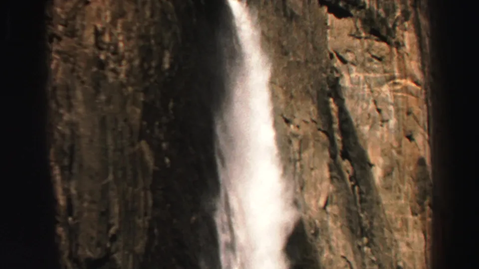 1969 Lake Tahoe 8mm frame showing a narrow white waterfall descending along a steep jagged cliff.