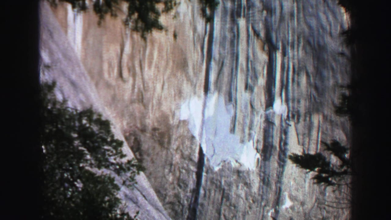 1969 Lake Tahoe 8mm frame showing a pale waterfall and steep cliff partly obscured by dark foreground trees.