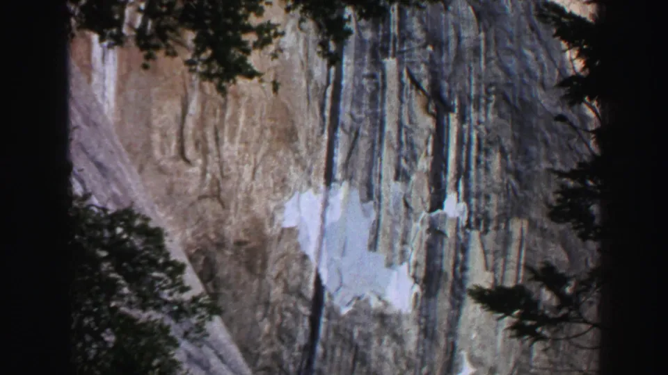 Lake Tahoe home-movie view of a waterfall descending across a cliff face, framed by dark trees and hanging vegetation.