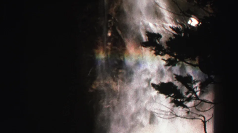 Lake Tahoe waterfall spray fills the frame with a faint rainbow and dark foreground branches in a late-1960s 8mm home movie.
