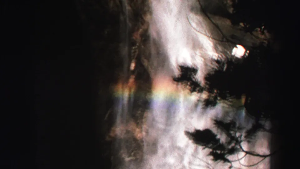 1969 Lake Tahoe 8mm frame showing waterfall spray, silhouetted trees, and a faint rainbow through mist.