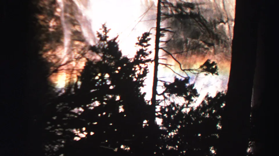 Lake Tahoe waterfall scene on 8mm film, with bright mist, dark tree shapes, and rainbow color near the spray.