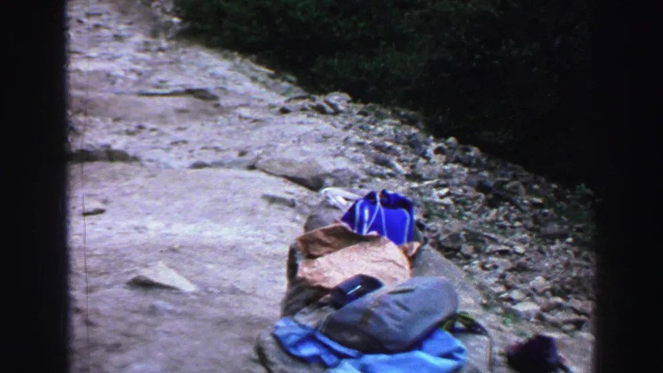 1969 Lake Tahoe trail view with blue camping gear and bags set on the edge of a rocky forest path.