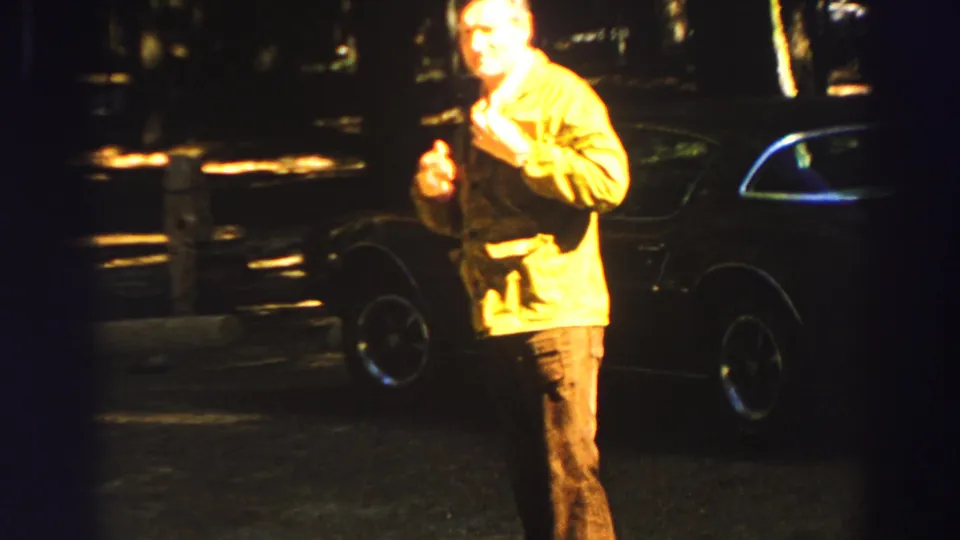 Adult man in a yellow jacket looks toward the camera while searching his pockets near a car at Lake Tahoe in 1969.