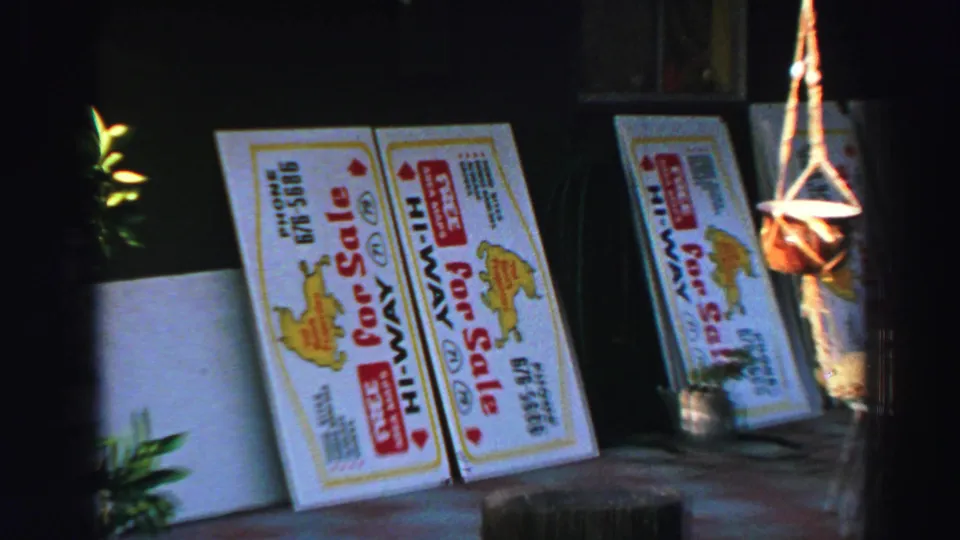 1969 Lake Tahoe frame with two bold white sale boards leaning against a dark wall beside plants and a hanging holder.