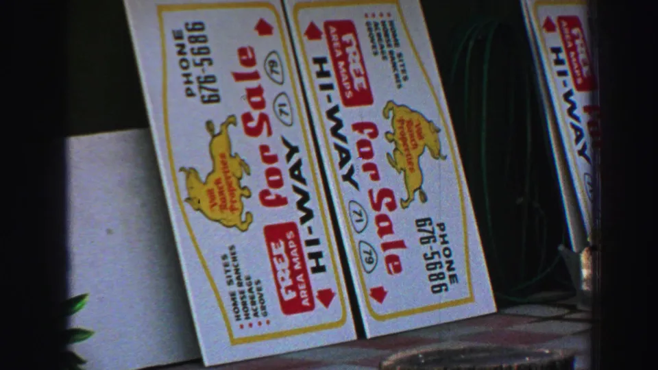 1969 Lake Tahoe close frame showing several leaning sale boards with red lettering, phone numbers and a yellow logo near plants.