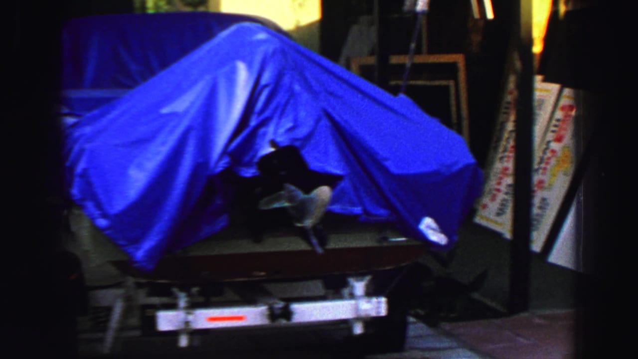 1969 Lake Tahoe frame showing a blue-covered boat on a trailer near sidewalk sale signs and shaded storefront materials.