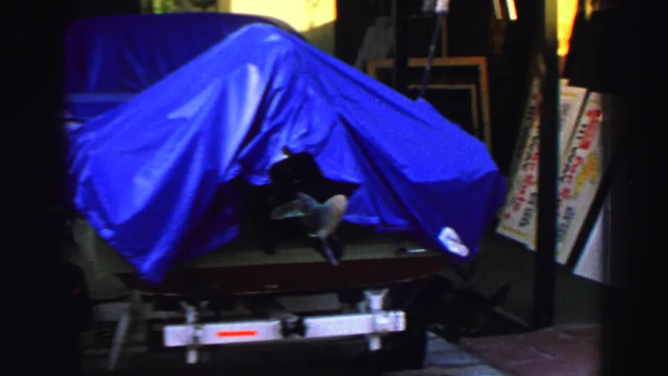 1969 Lake Tahoe frame showing a blue-covered boat on a trailer near sidewalk sale signs and shaded storefront materials.
