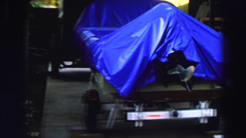 1969 Lake Tahoe 8mm frame showing a boat covered with a vivid blue tarp on a trailer near trees and driveway shade.