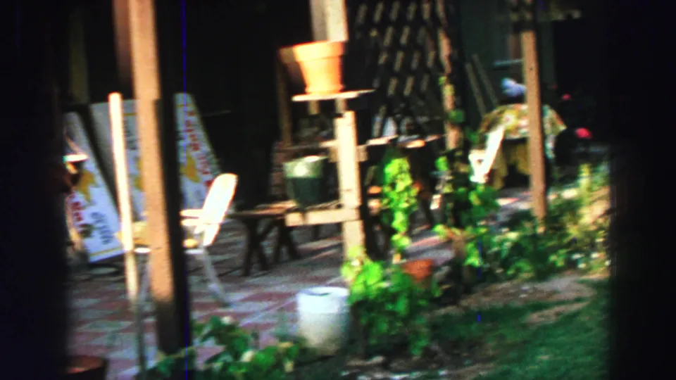 Lake Tahoe home-movie frame showing a shaded patio with chairs, potted plants, and real-estate signs leaning against the structure.