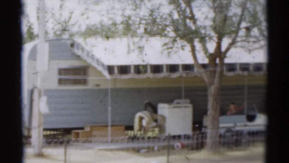 1959 8mm view of a Disneyland, California trailer area with awning, washer, tree, fence, and an indistinct person by the mobile home.