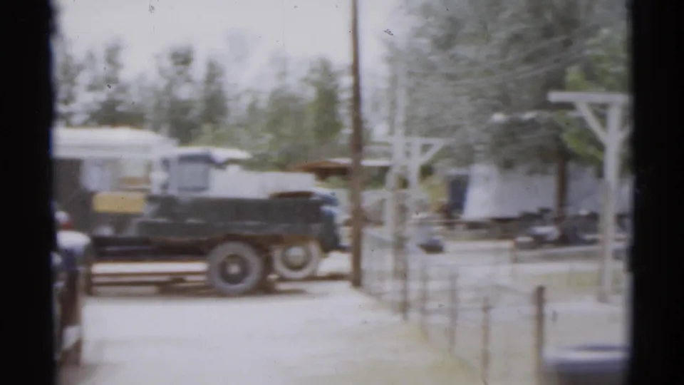 1959 8mm view of a dark older truck near trailers, fence posts, trees, and utility elements in the stated Disneyland, California setting.