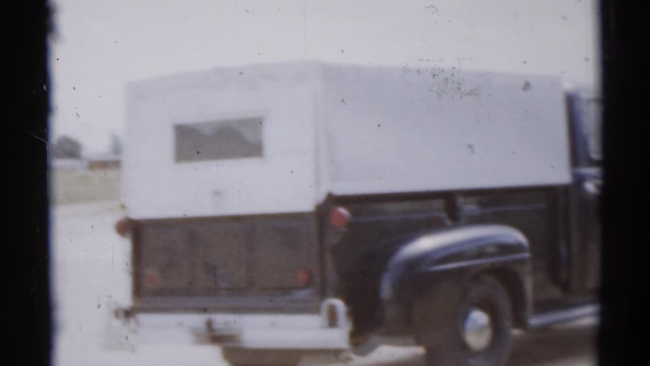 Black pickup truck with a white camper shell parked in an open lot.
