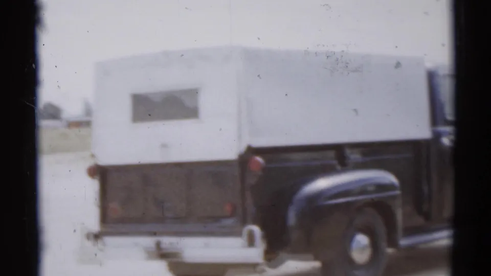 1959 Disneyland home-movie frame showing a black pickup with a white camper shell in a parking area.