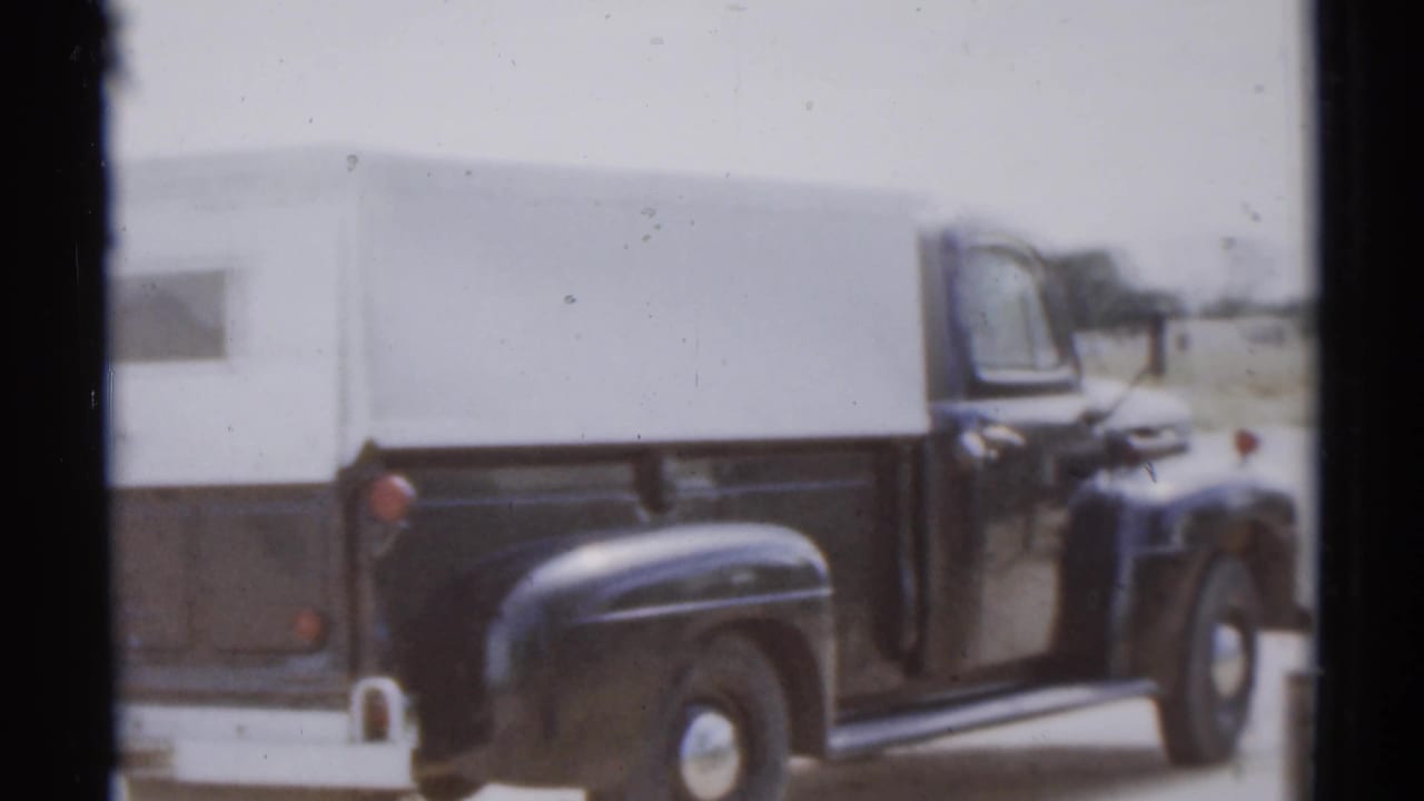Side view of a black pickup and white camper shell in the Disneyland parking area, filmed on 8mm in 1959.