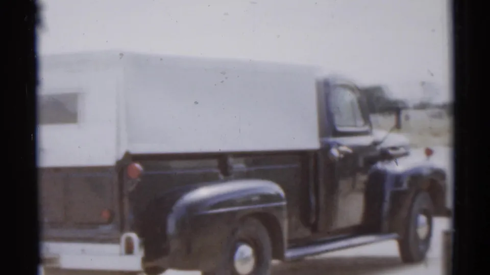 Side view of a black pickup and white camper shell in the Disneyland parking area, filmed on 8mm in 1959.