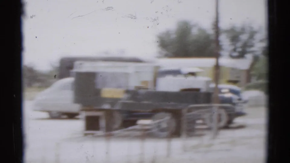 Blurred 1959 home-movie view of a trailer and parked vehicles near the Disneyland parking area.