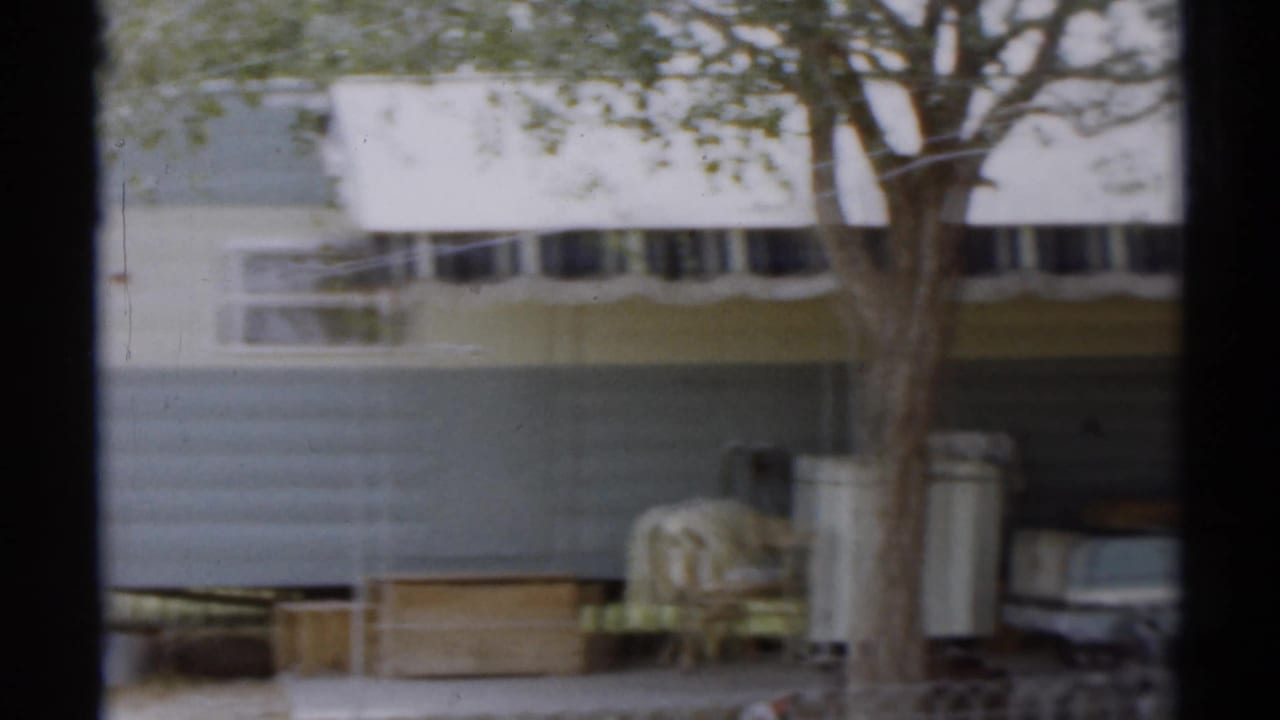 Striped awning over a trailer-like building with trees and a pale parked car.