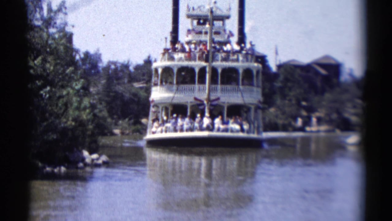 White multi-deck riverboat approaches on a tree-lined waterway with passengers visible on deck.