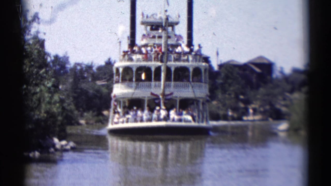 Riverboat moves closer on the water, framed by trees and dark film borders.