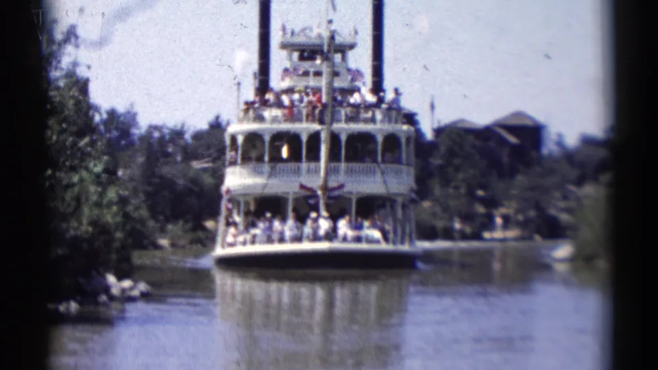 Visitor-shot 8mm view of a crowded Disneyland riverboat approaching through a landscaped waterway in 1959.