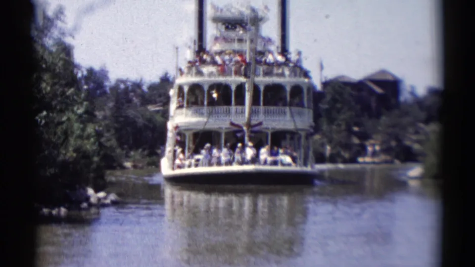 The white Disneyland riverboat remains centered as passengers gather on open decks during the 1959 scenic ride.