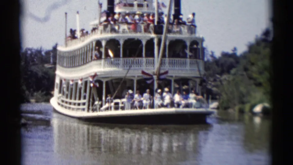 Closer 1959 Disneyland view of the paddlewheel-style riverboat passing on the water, with passengers visible across both decks.
